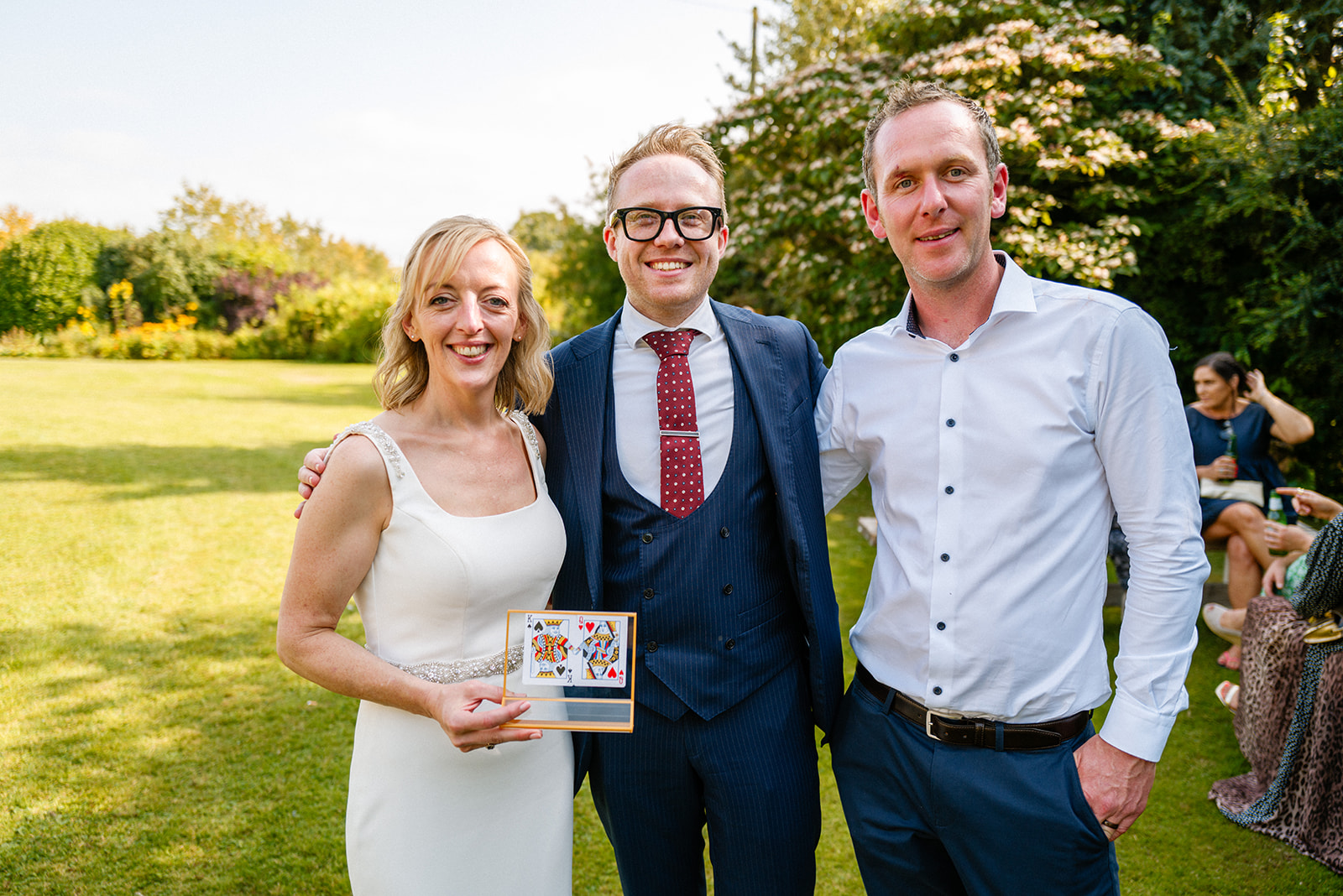 Couple holding a framed card-trick keepsake with Kristian at a garden wedding